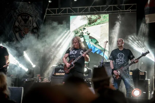 Live rock music performance at a festival with energetic musicians playing guitars on stage surrounded by lights and smoke